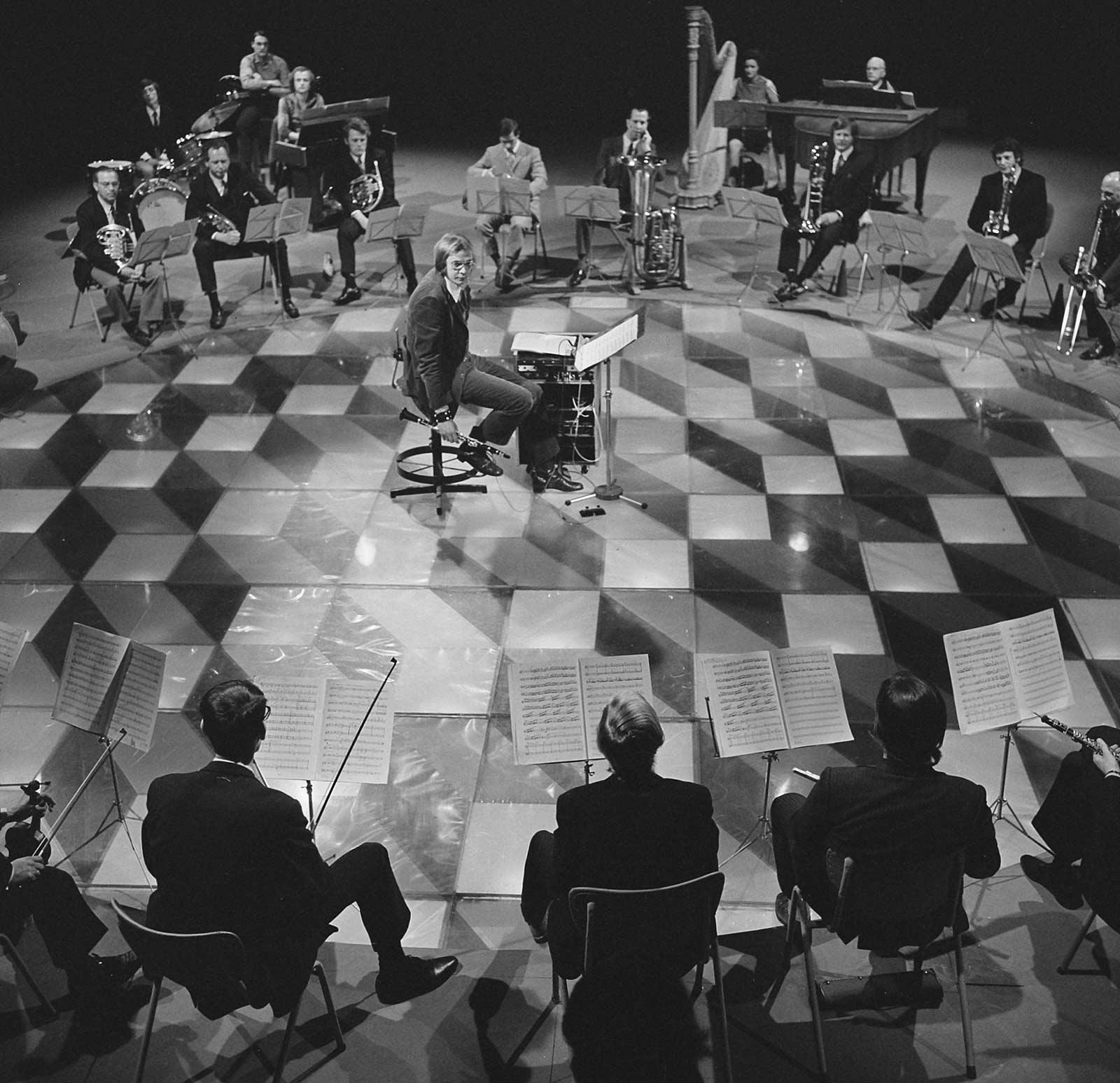 Still image from the tv recording by the NCRV of Time Spirit. Seated in the middle is clarinet player George Pieterson, members of the Rotterdam Philharmonic Orchestra surround him. Photo: Nederlands Instituut voor Beeld en Geluid